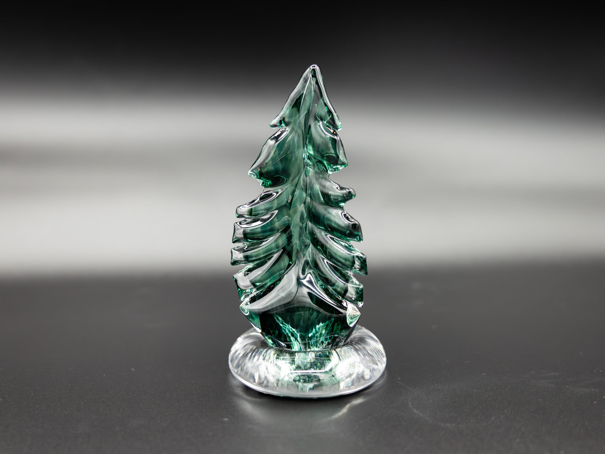 Small green glass tree figurine on a reflective surface with a dark background