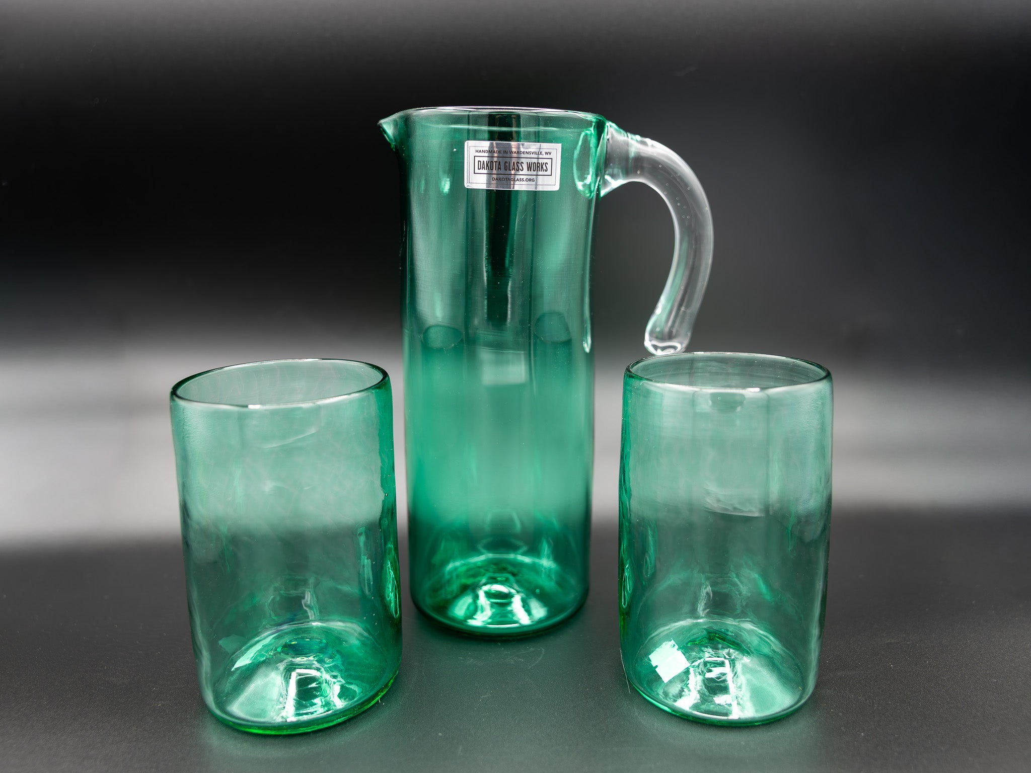 Green glass pitcher and two glasses on a dark background
