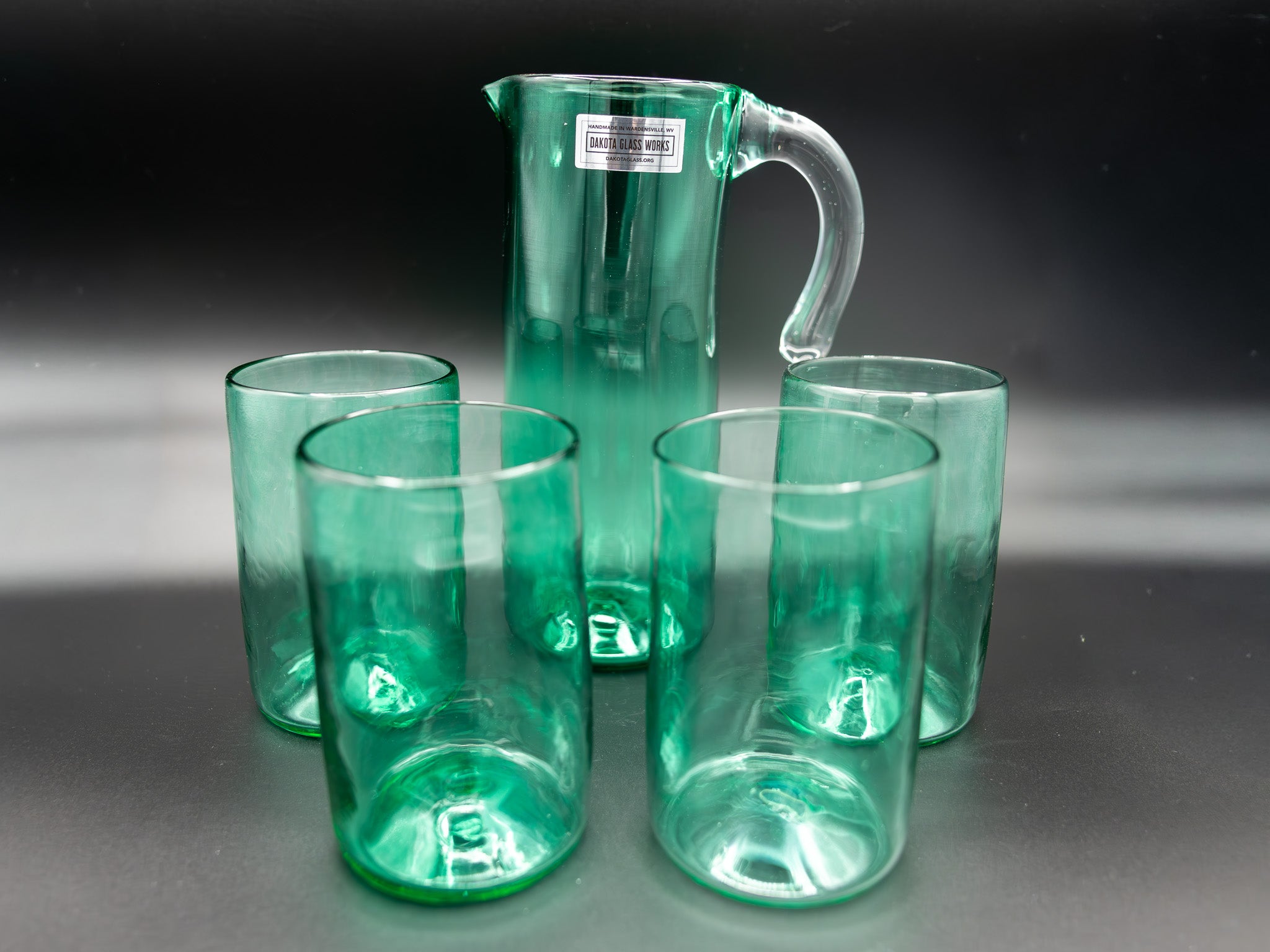 Set of green glass tumblers and a pitcher on a dark background