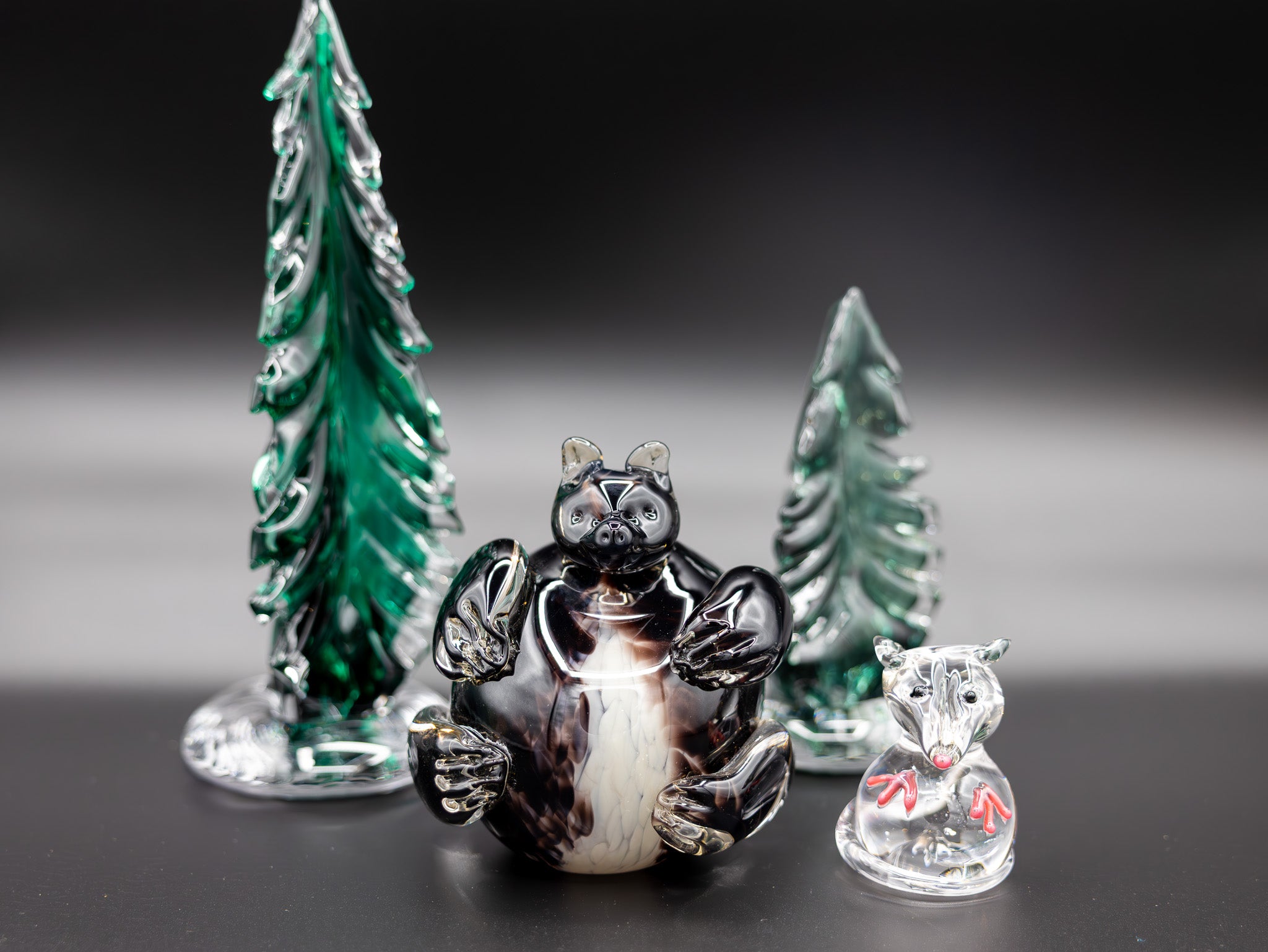 two glass trees, a glass bear, and glass opossum on a dark background