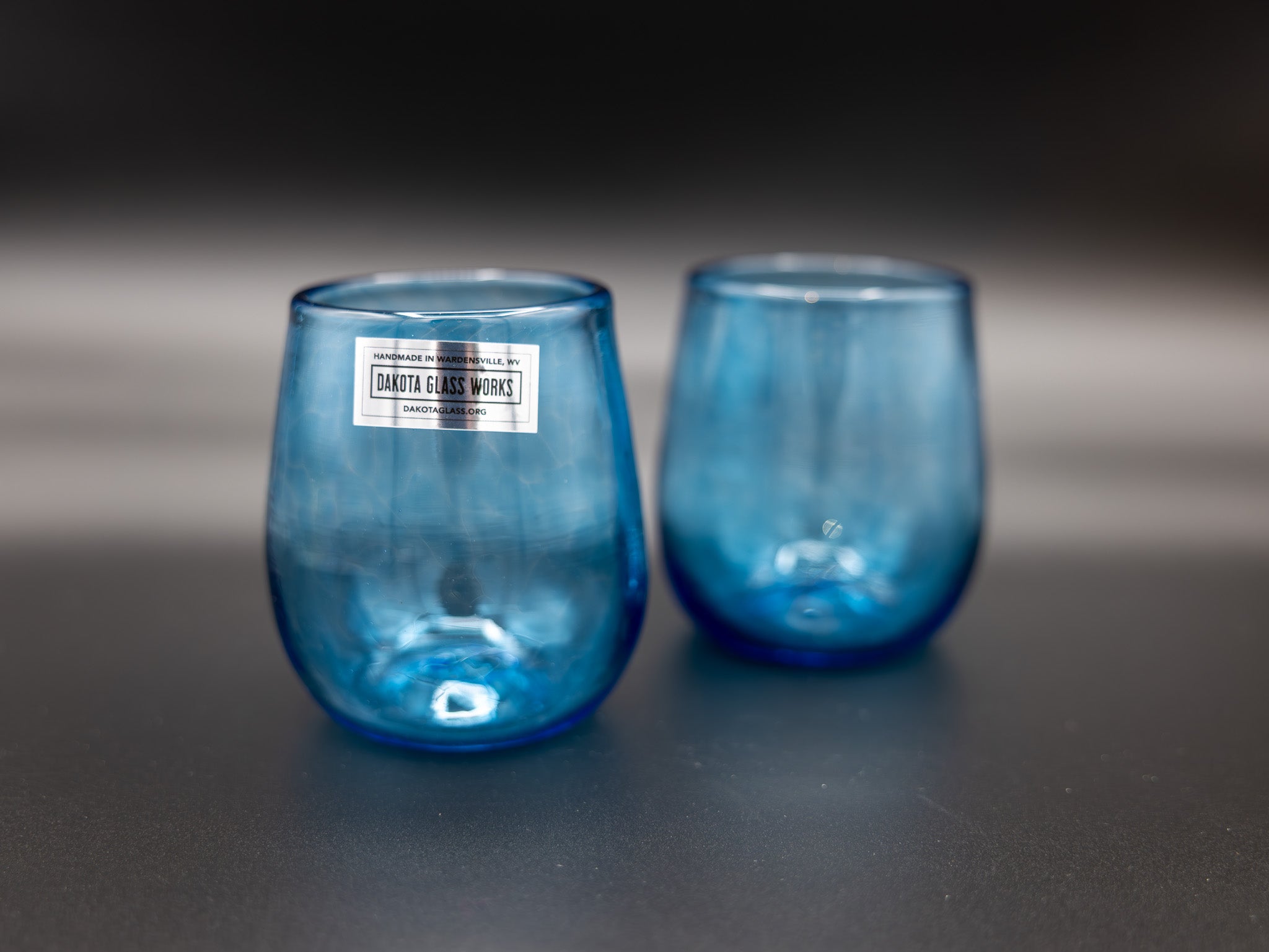 Two blue stemless wine glasses on a dark surface with a blurred background