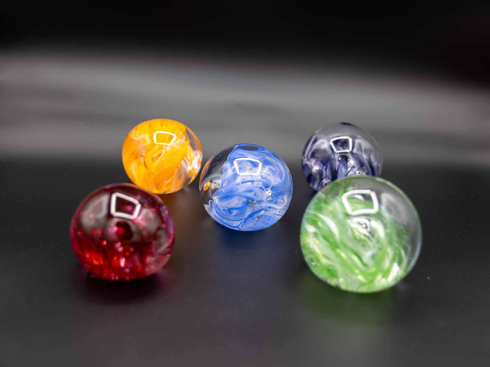 Five colorful glass paperweights on a dark surface