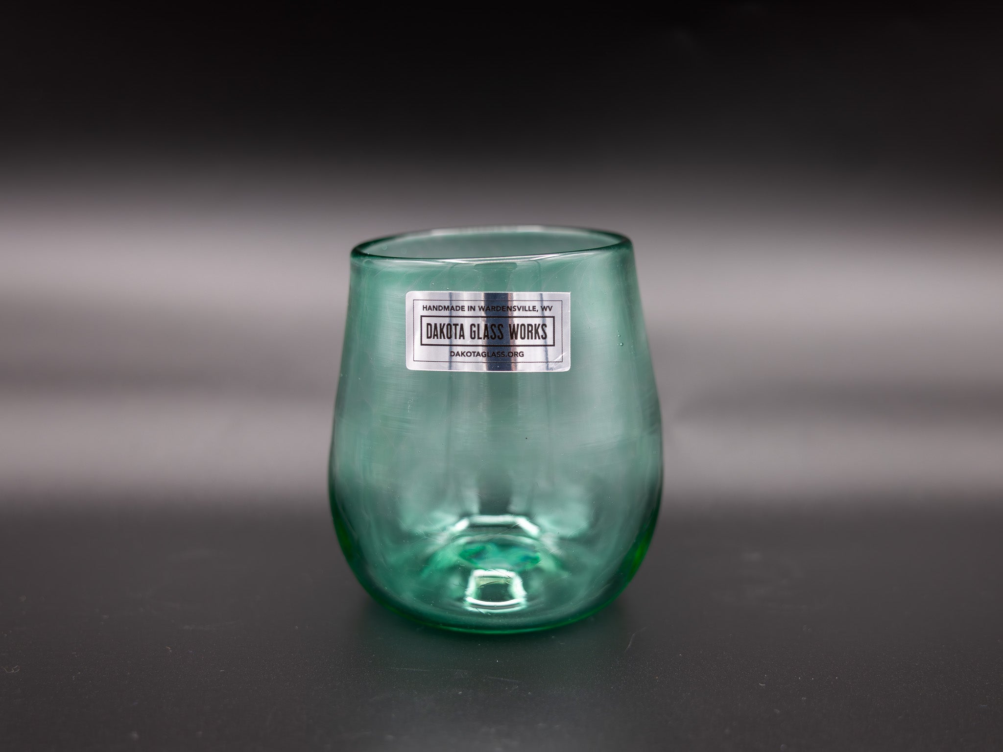 Green stemless wine glass with a label on a dark background