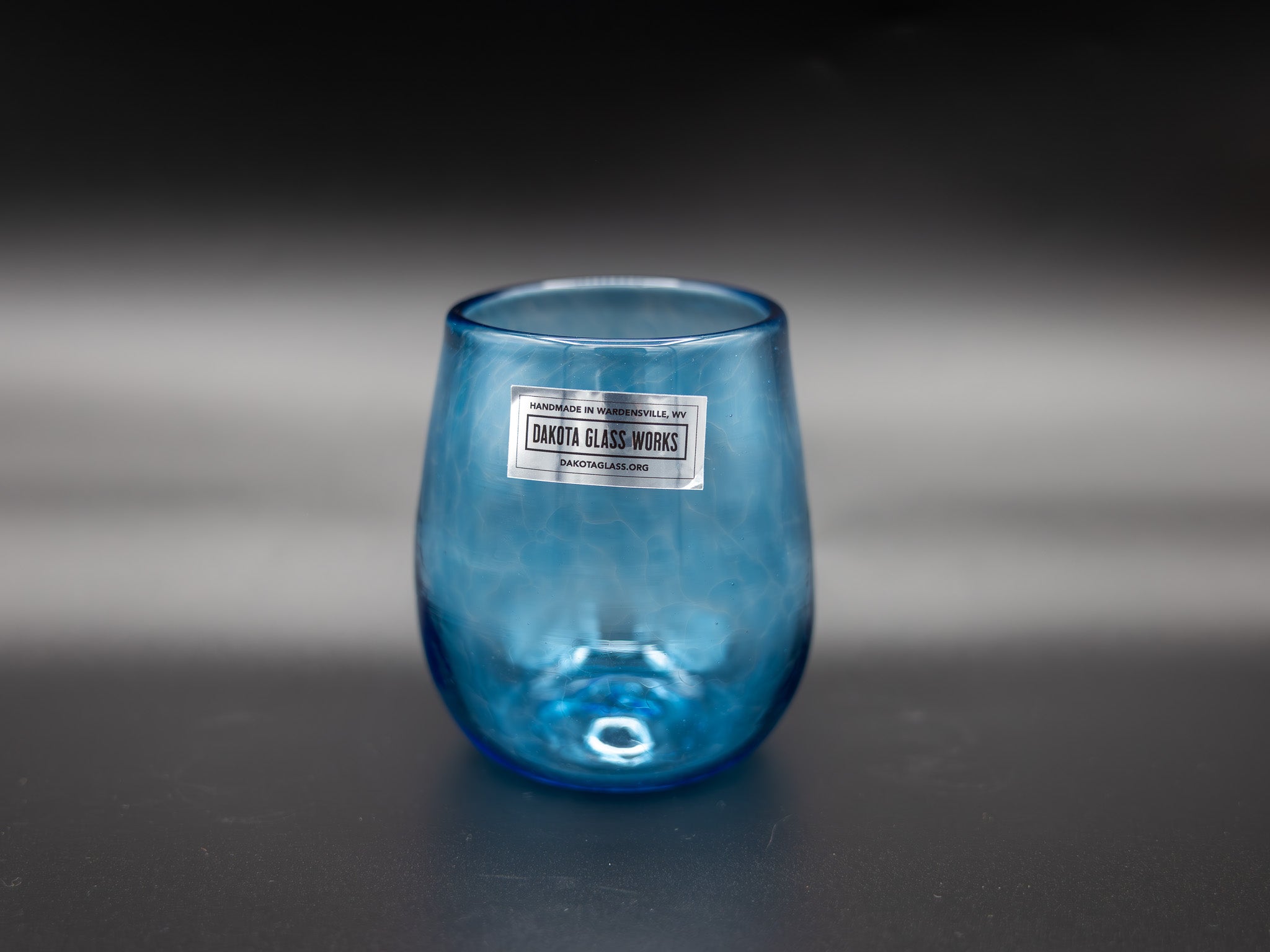Blue stemless wine glass with a label on a dark background