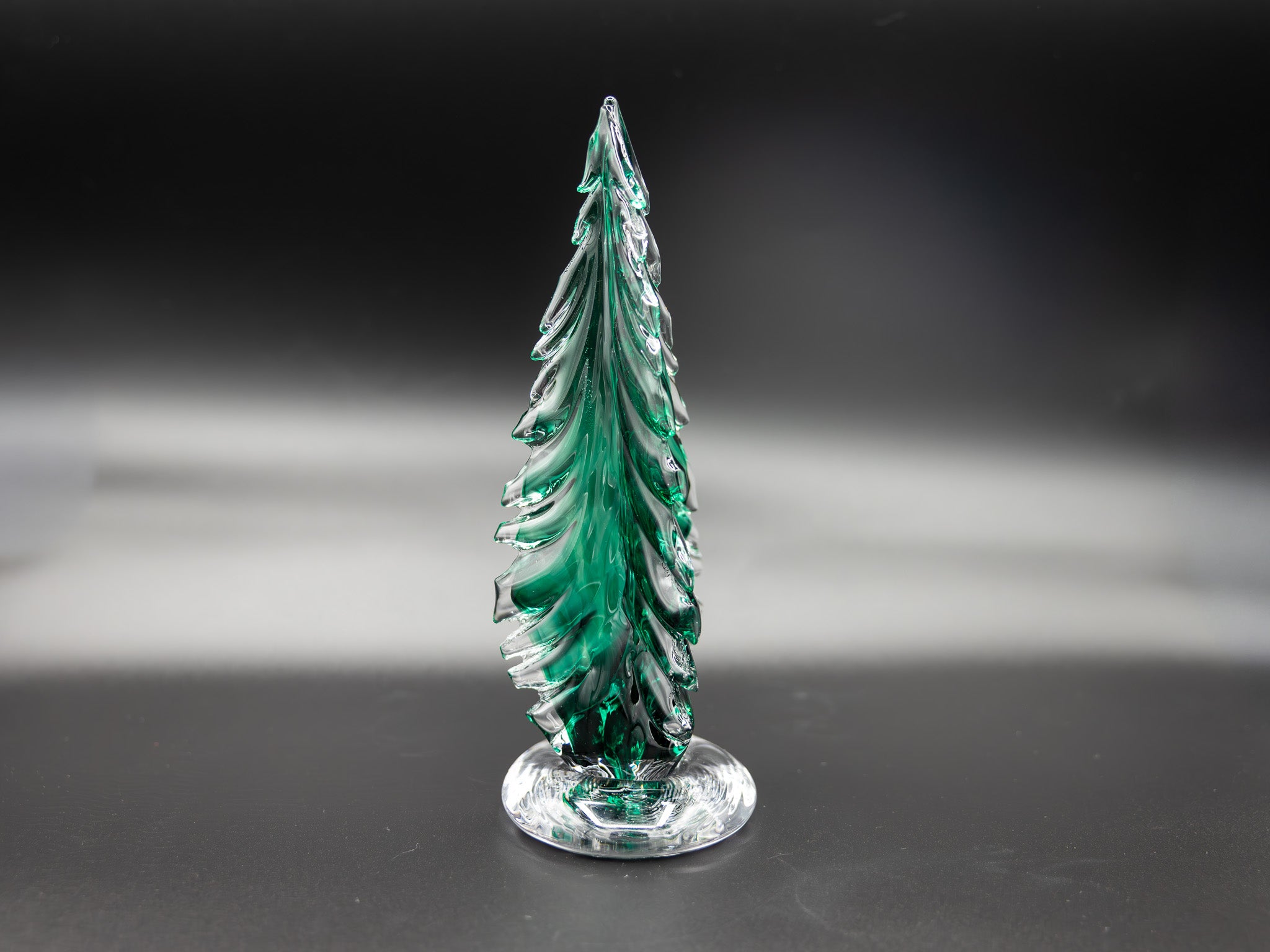 Large green glass tree on a reflective surface with a dark background