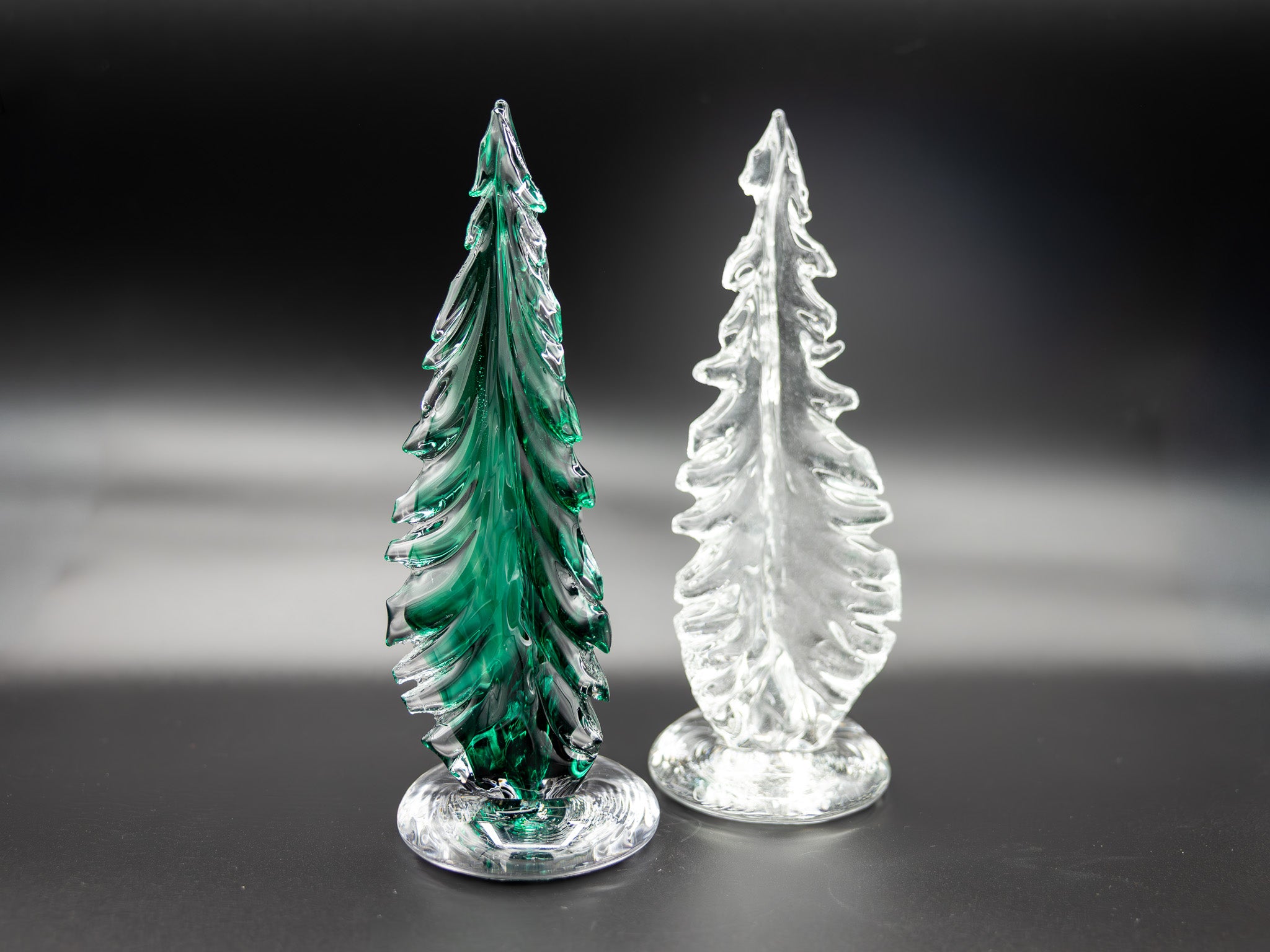 Two glass trees, one green and one clear, on a dark background