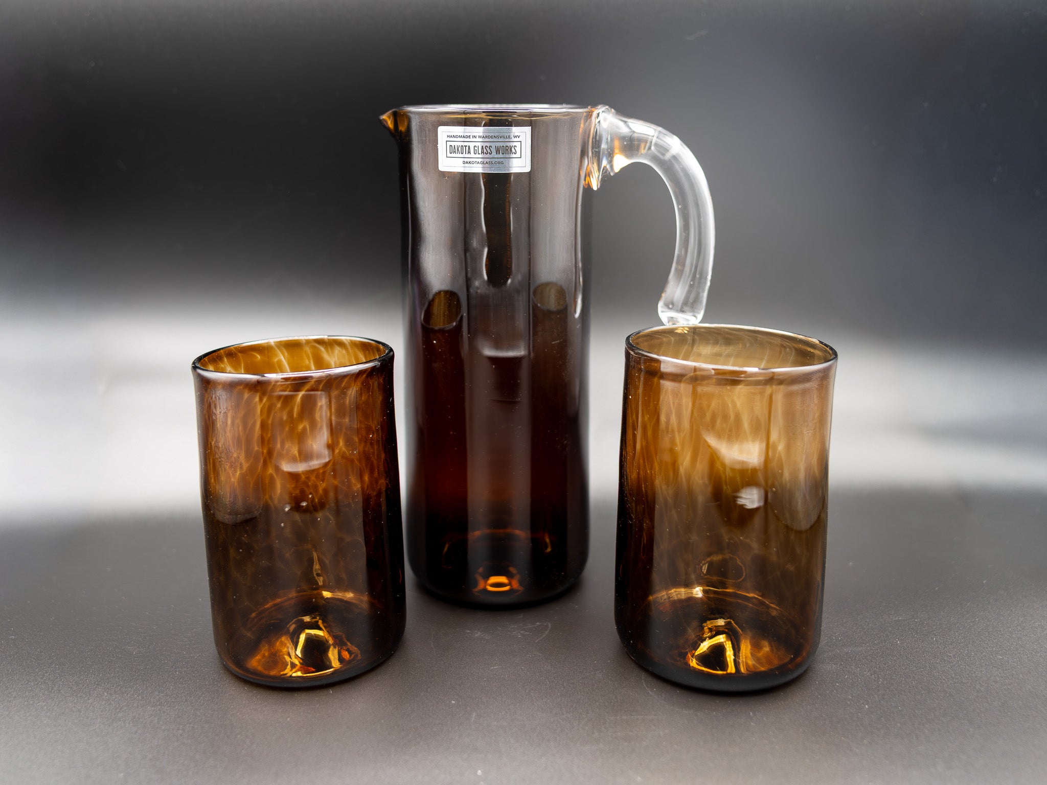 Set of three brown glass pieces including a pitcher and two tumblers on a gray background