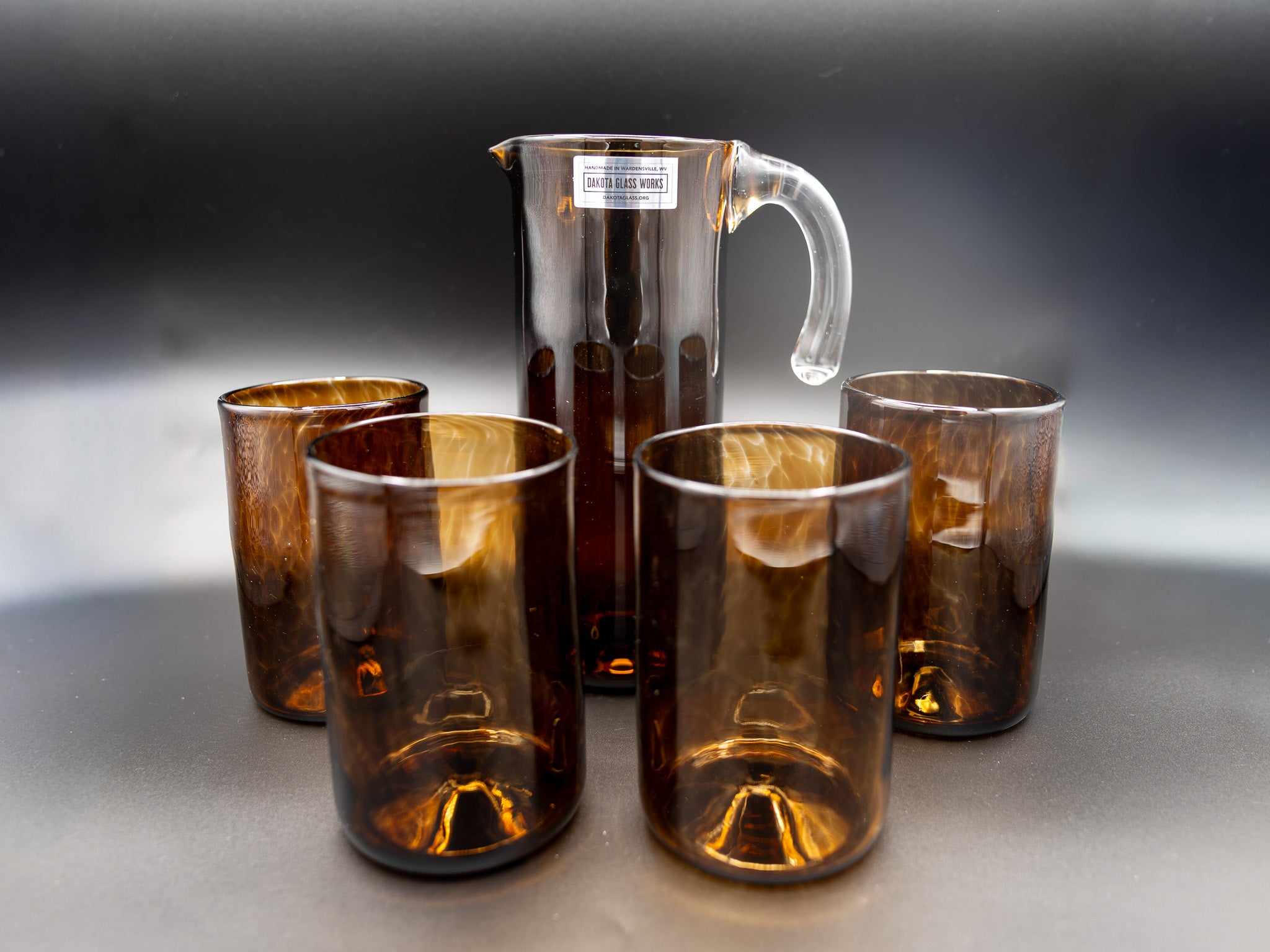 Set of brown glass tumblers and a pitcher on a gray surface with a dark background