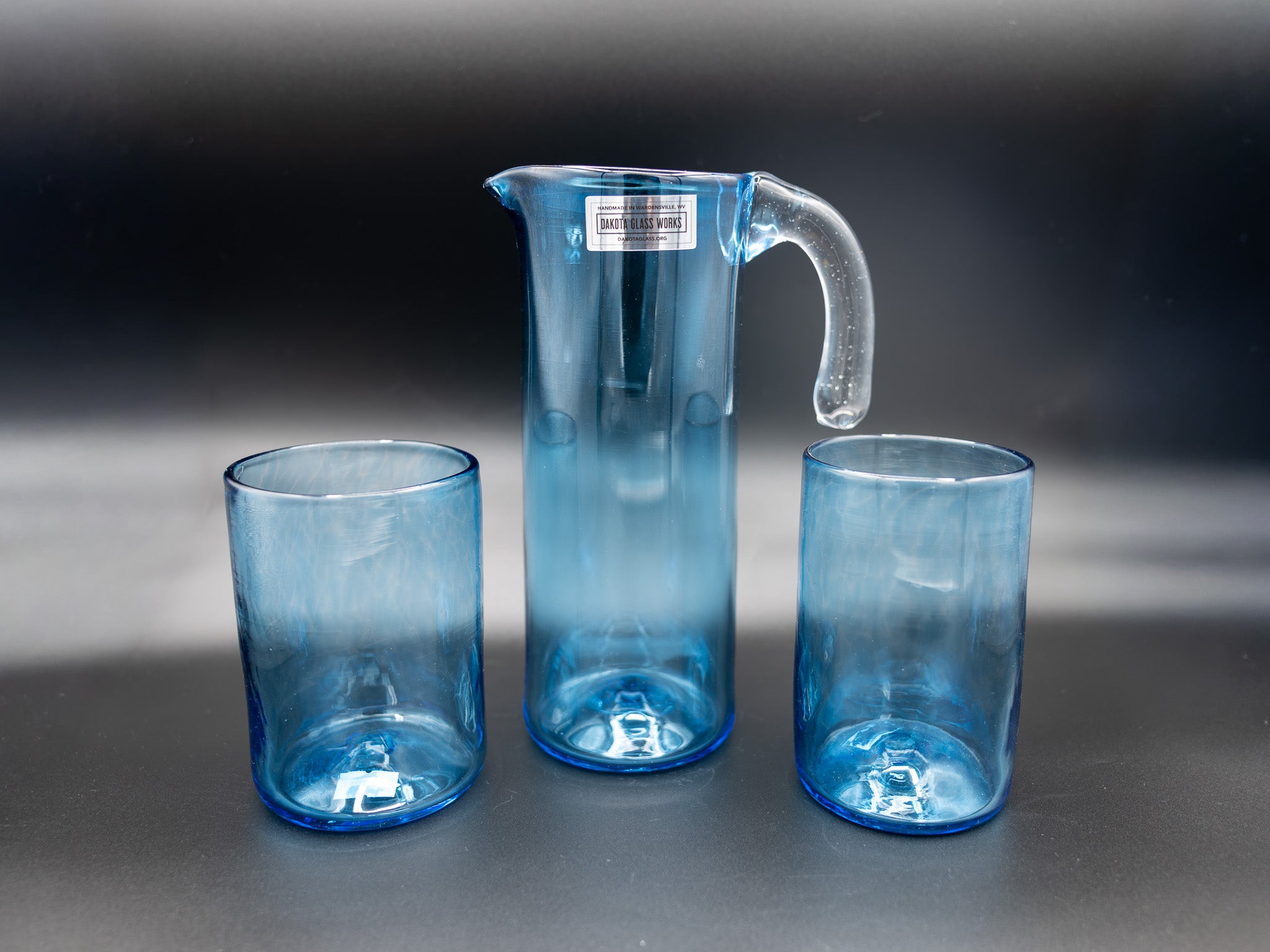 Set of two blue glass tumblers and a matching pitcher on a dark background