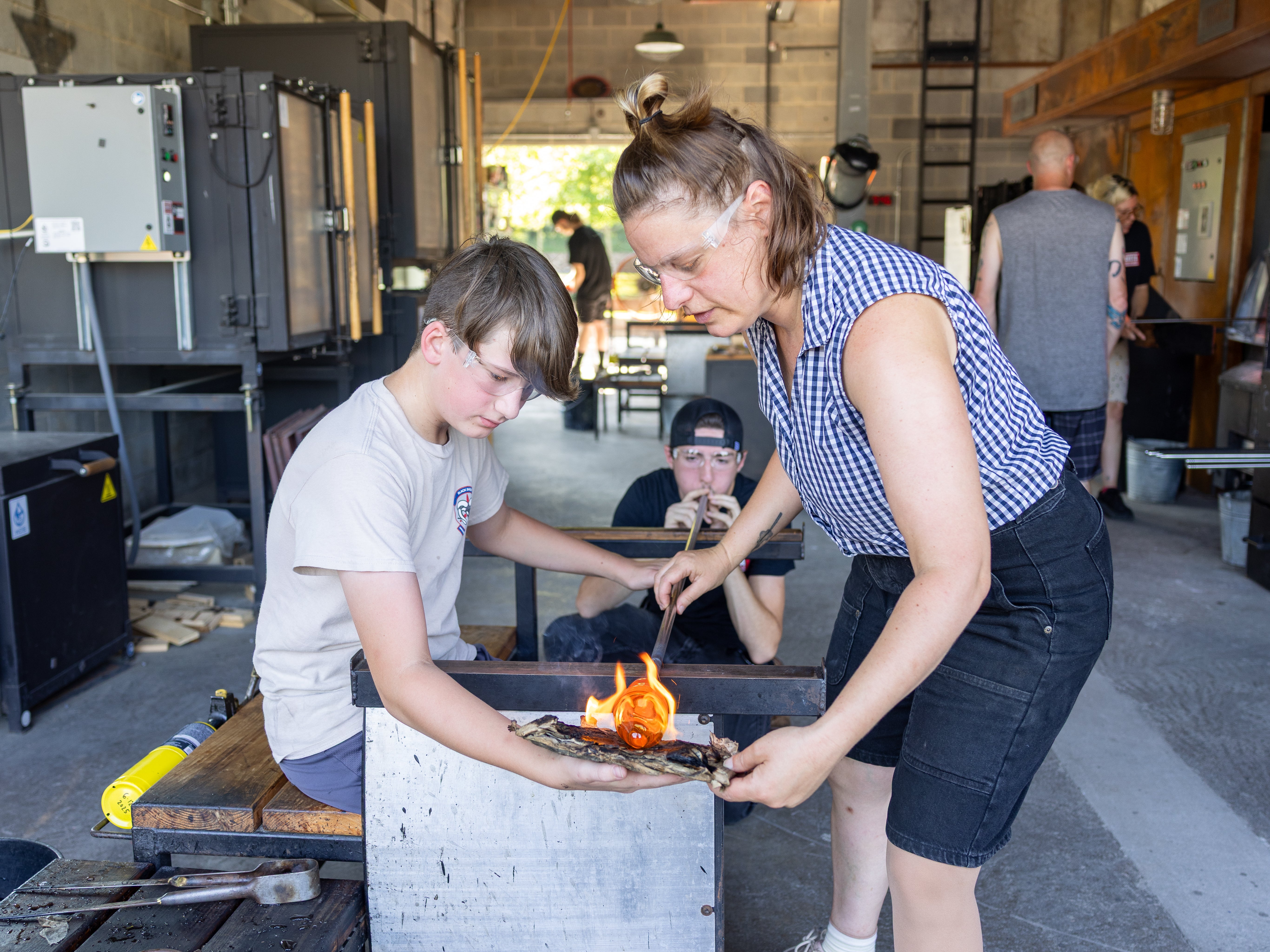 Two people working on a handblown cup  in a workshop setting