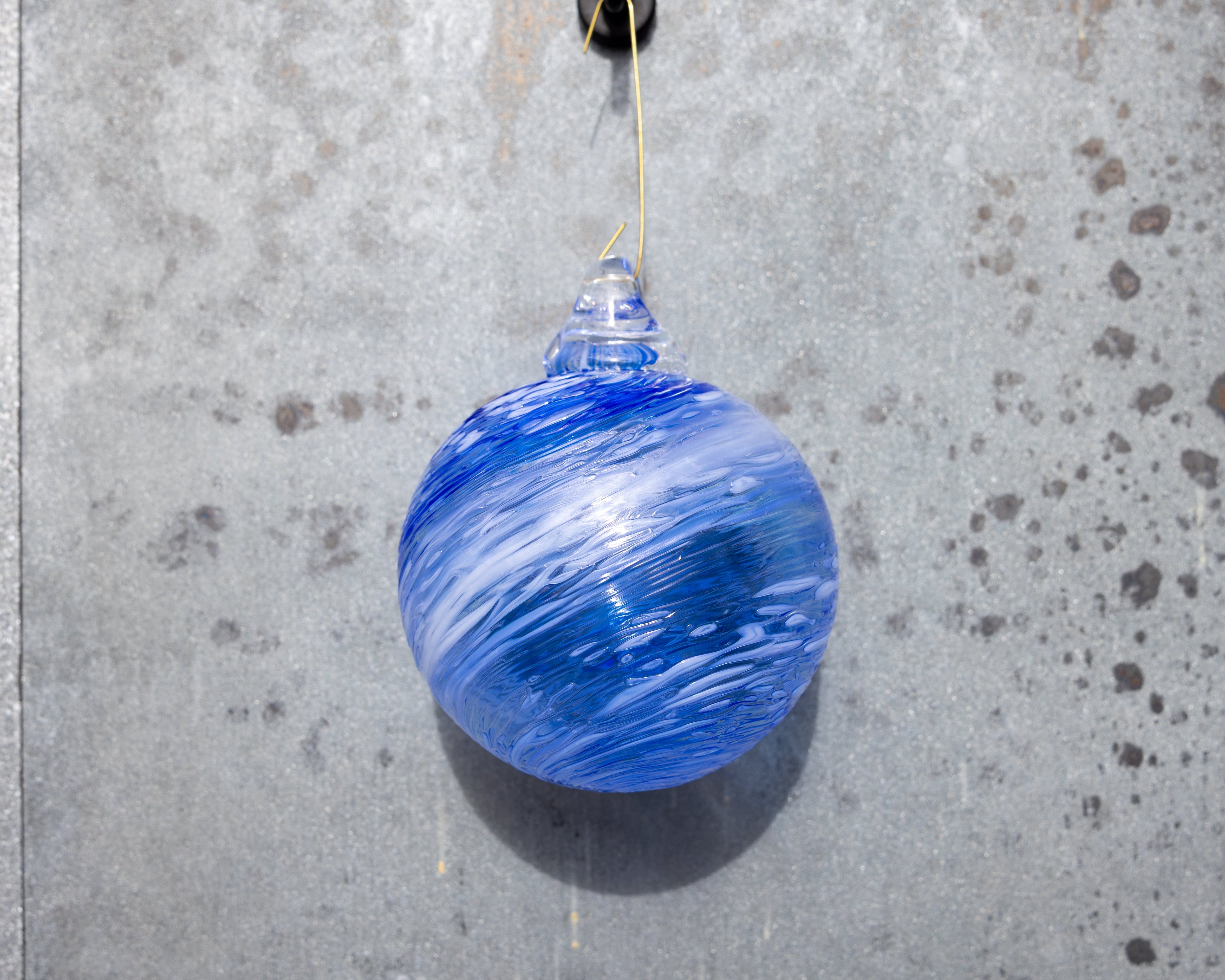 Blue glass ornament hanging on a textured gray wall