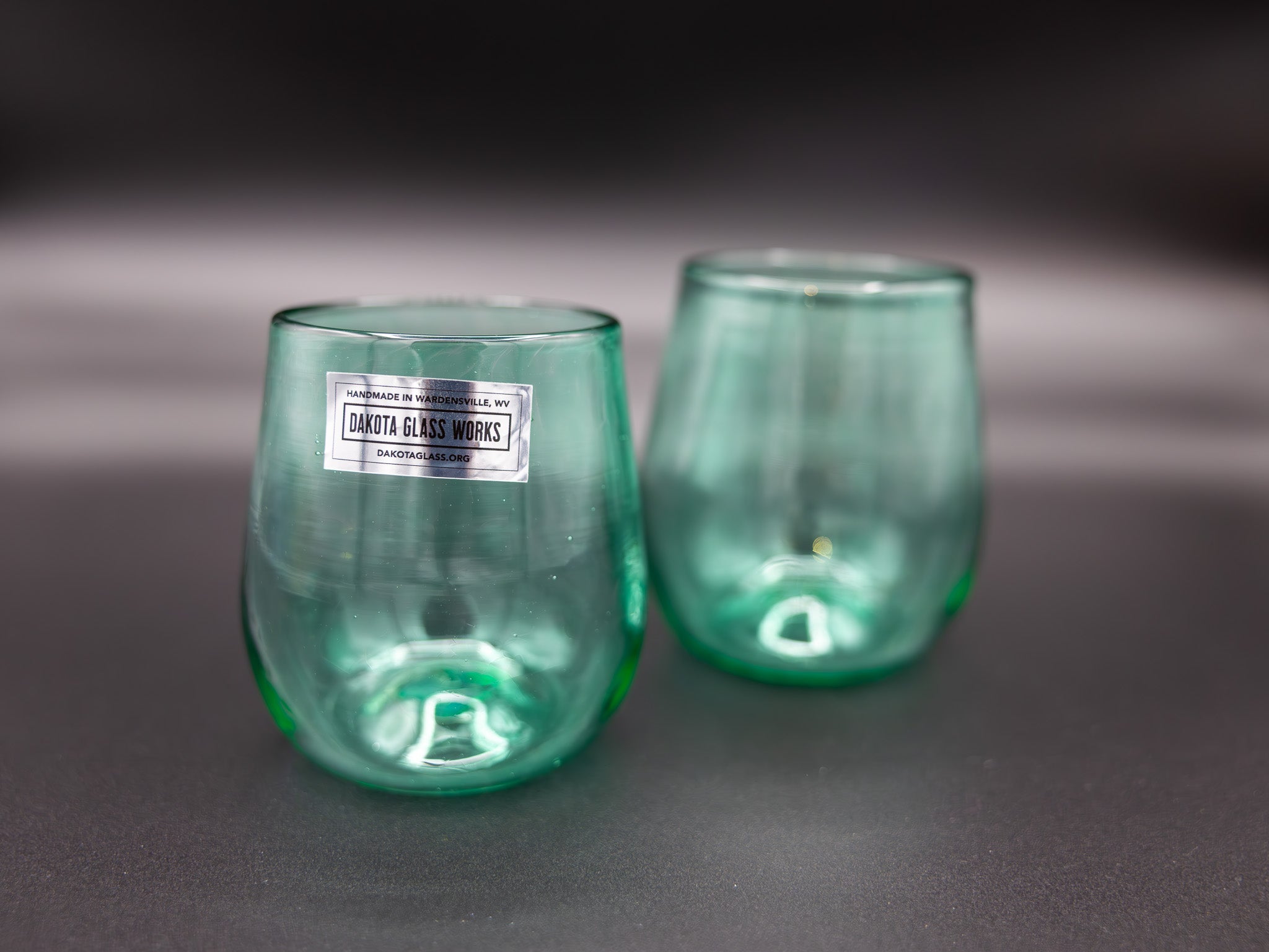 Two green stemless wine glasses with a visible brand label on a dark background