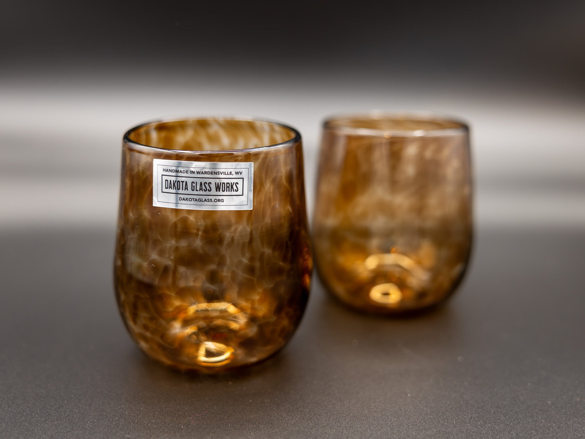Two brown stemless wine glasses with a visible label on a gray background