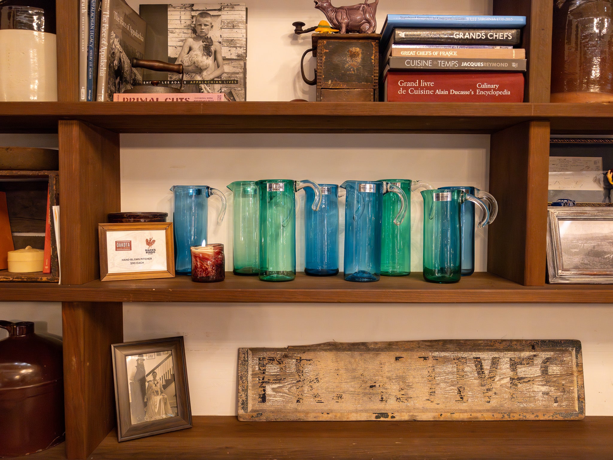 Wooden shelf with colorful pitchers, framed photos, and decorative items.