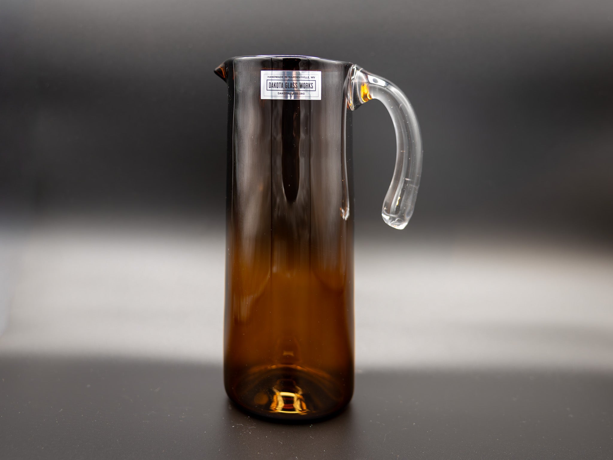 Brown glass pitcher with a clear handle on a dark background