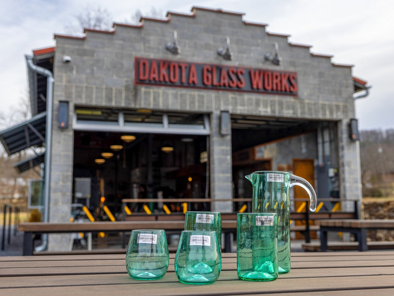 Green glassware on a table with Dakota Glass Works building in the background