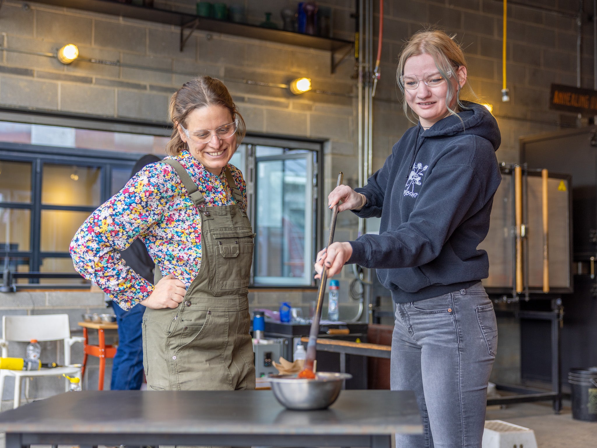 Alex observing a guest dip a punty into a bowl of frit to gather color