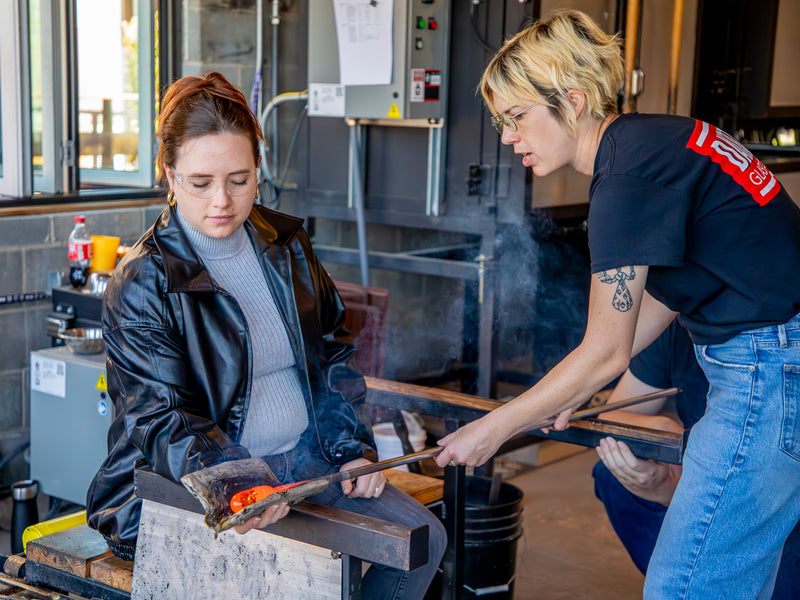 Two people working with glassblowing tools during a workshop.
