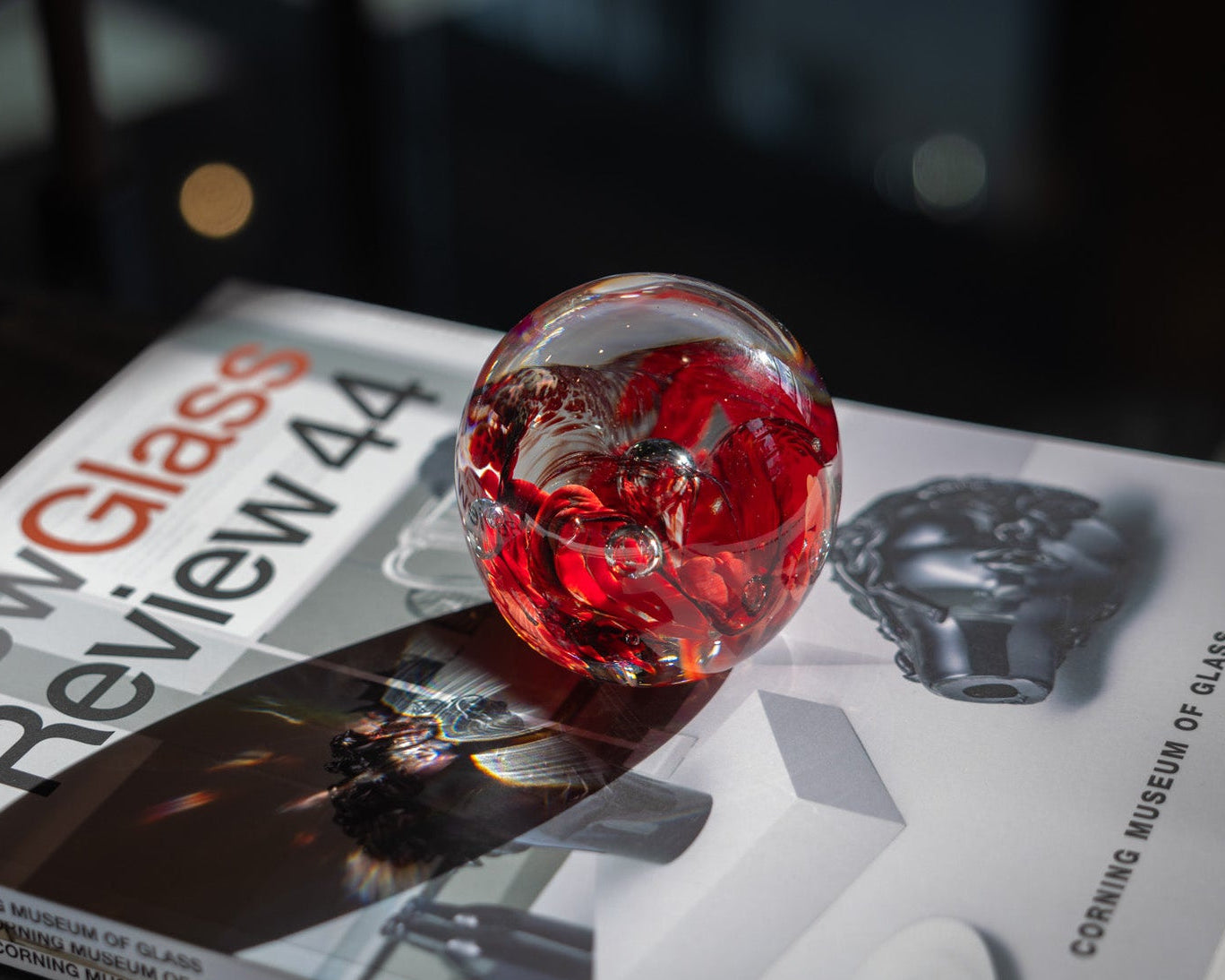 Red glass paperweight on a magazine with 'Glass Review' visible