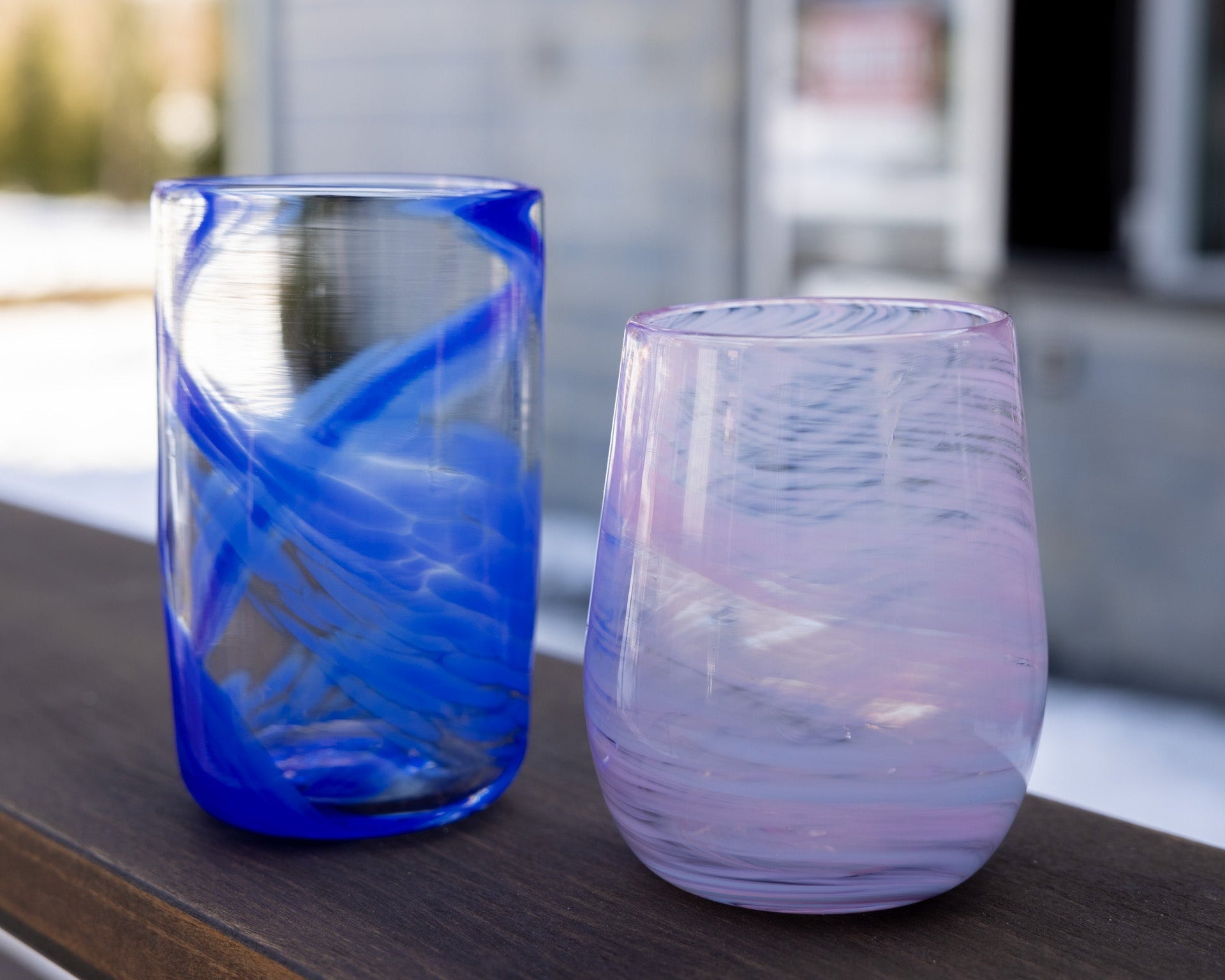 Two glasses, one blue and one purple, on a wooden surface with a blurred background.