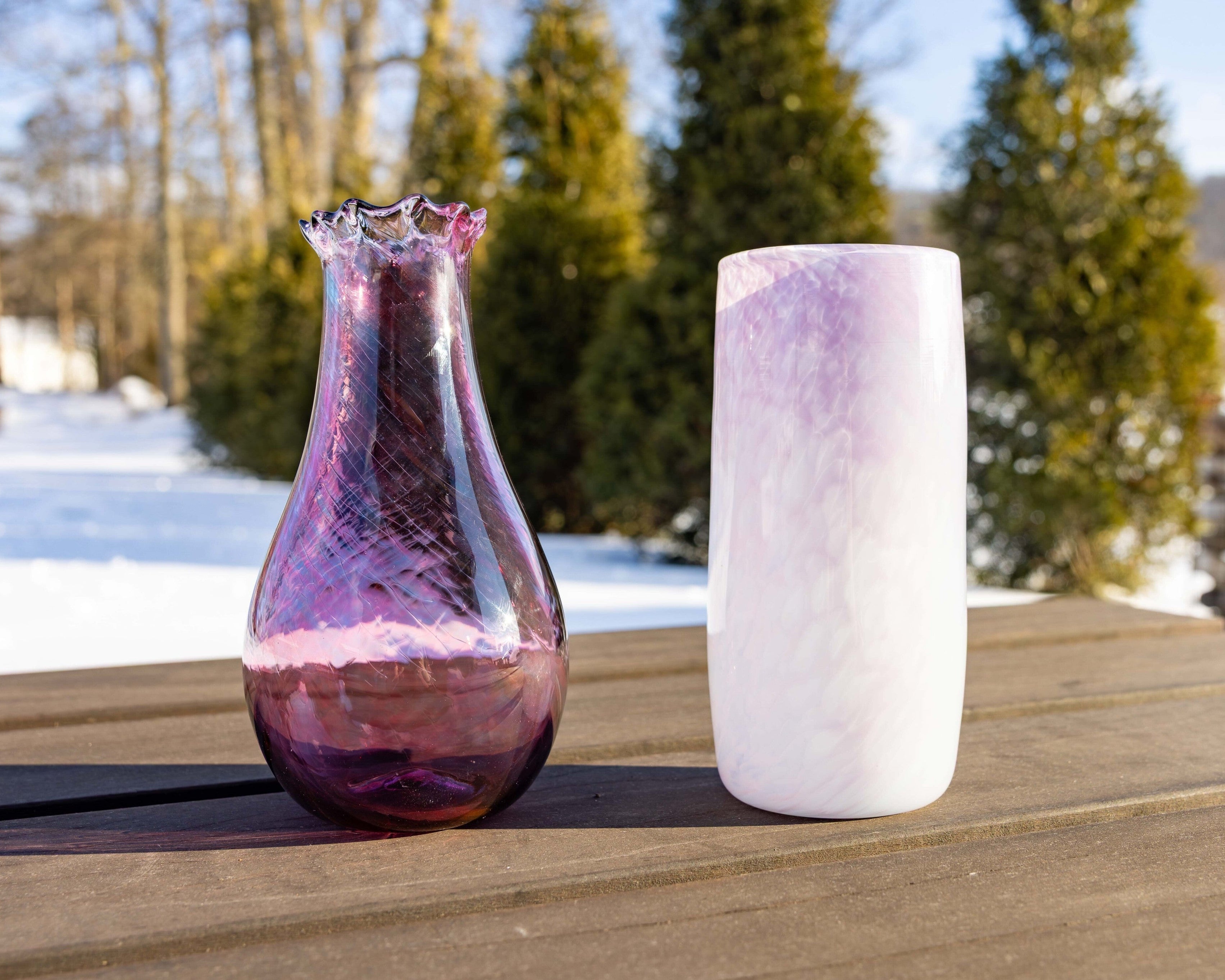 Two glass vases on a wooden surface with a snowy landscape in the background