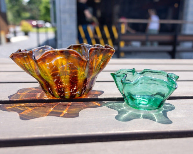 Two glass bowls, one brown and one green, on a wooden surface with a blurred outdoor background.